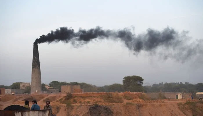 This picture shows smoke billowing from a chimney as Pakistani labourers rest beside a brick kiln. — AFP/File