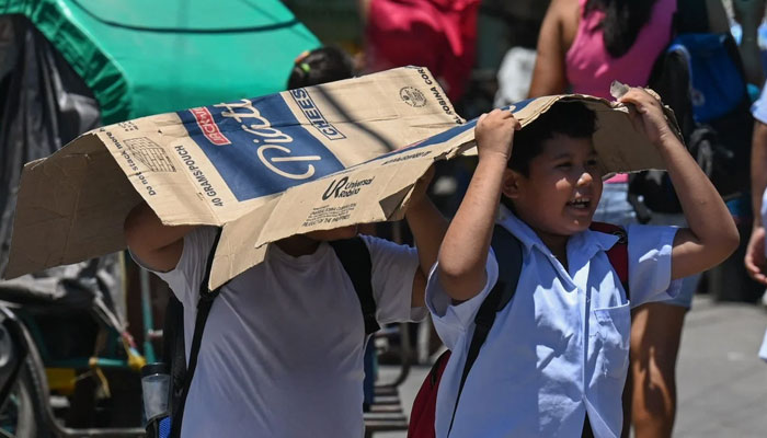 Students use cardboard to protect themselves from the sun during a hot day in Manila. — AFP/File