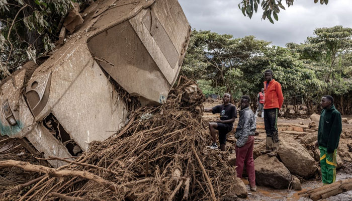 Young men inspect a destroyed car carried by waters in an area heavily affected by torrential rains and flash floods in the village of Kamuchiri, near Mai Mahiu, on 29 April 2024. — AFP