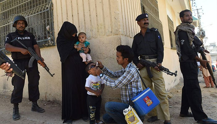 A representational image showing policemen standing guard as a health worker administers polio drops to a child during a polio vaccination campaign. — AFP/File