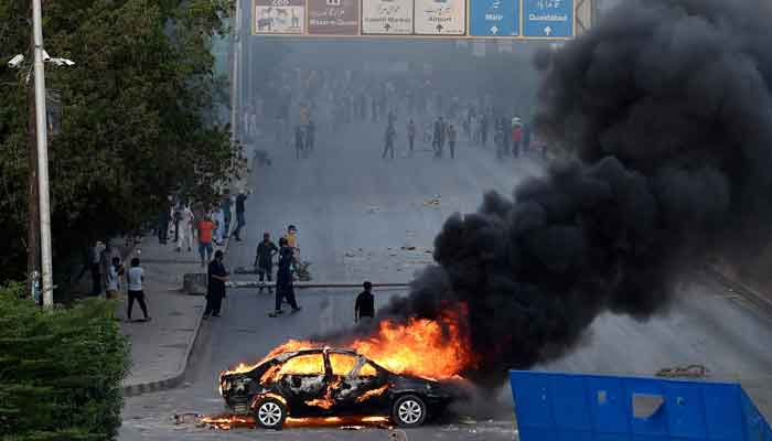 A car is seen burning along a road as Pakistan Tehreek-e-Insaf (PTI) party activists and supporters of former prime minister Imran Khan block a road during a protest against the arrest of their leader in Karachi on May 9, 2023. — AFP