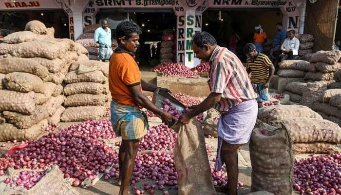 Labourers fill a bag with onions at a wholesale vegetable market in Chennai, India. — AFP/File