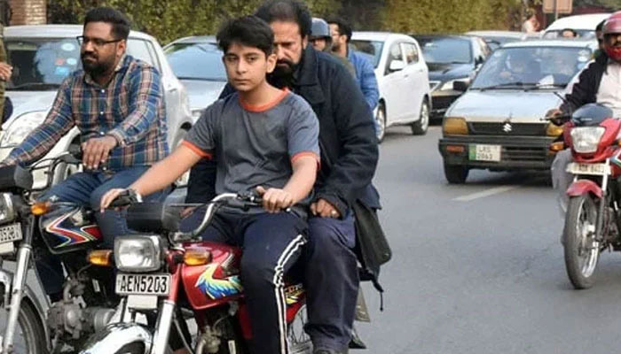A young boy is riding a motorcycle with his father seated with him on the way to a road in Lahore in November 19, 2023. — Online
