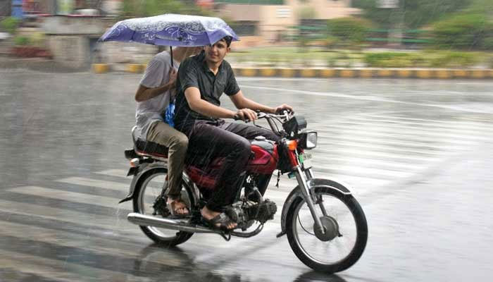 A motorcyclist and a pillion rider protect themselves with an umbrella during heavy rain in Lahore. — Online/File