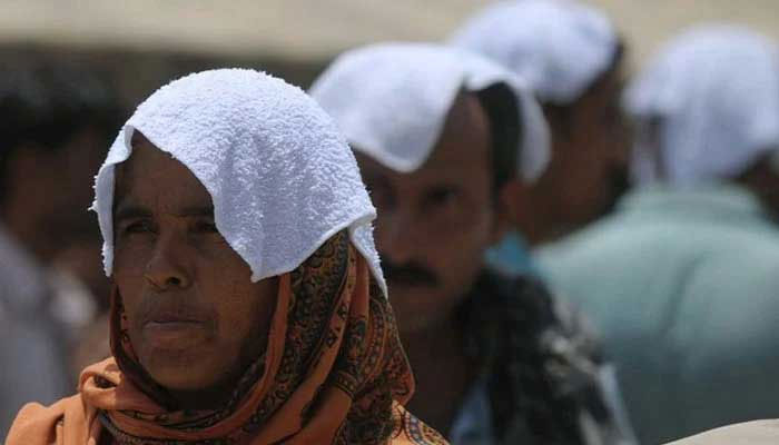 Pakistani relatives of heatstroke victims, their heads covered with wet towels, wait outside a hospital during a heatwave in Karachi. — AFP/File