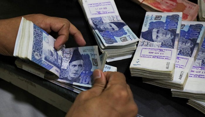 n employee counts Pakistani rupee notes at a bank in Peshawar on August 22, 2023. — Reuters
