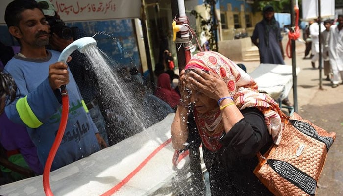 A volunteer showers a woman with water during a heat wave in Pakistan. — AFP/File