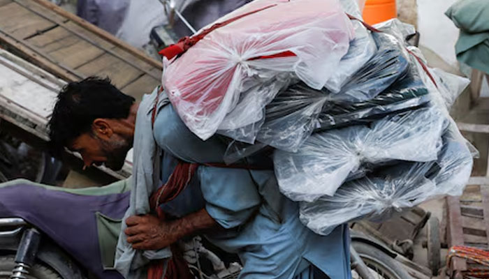 A labourer bends over as he carries packs of textile fabric on his back to deliver to a nearby shop in a market in Karachi on June 24, 2022. — Reuters