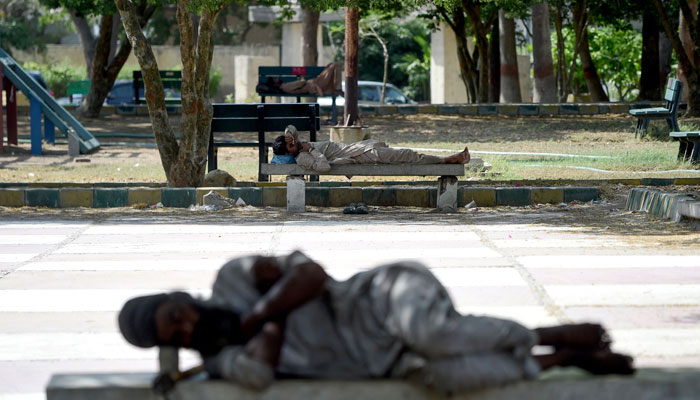 Men sleep on benches under the shade of trees at a park on a hot summer afternoon in Karachi on May 24, 2024. — AFP