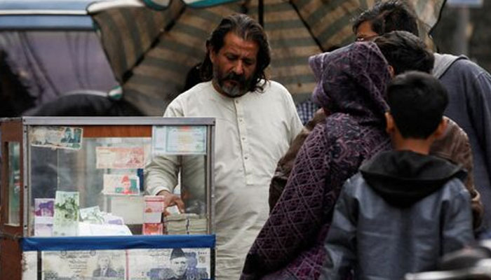 A currency broker stands near his booth, which is decorated with pictures of currency notes, while dealing with customers, along a road in Karachi, Pakistan January 27, 2023. — Reuters