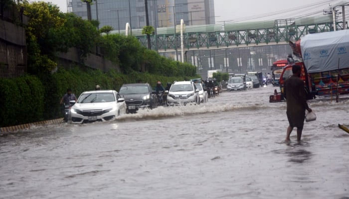 Vehicles crossing road flooded with rainwater after heavy rain in Lahore on July 22, 2023. — APP