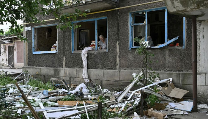 Lyudmila, 68, looks out of a blown window of her flat in a damaged residential building following overnight Russian strike in the town of Selydove, Donetsk region on June 14, 2024. — AFP