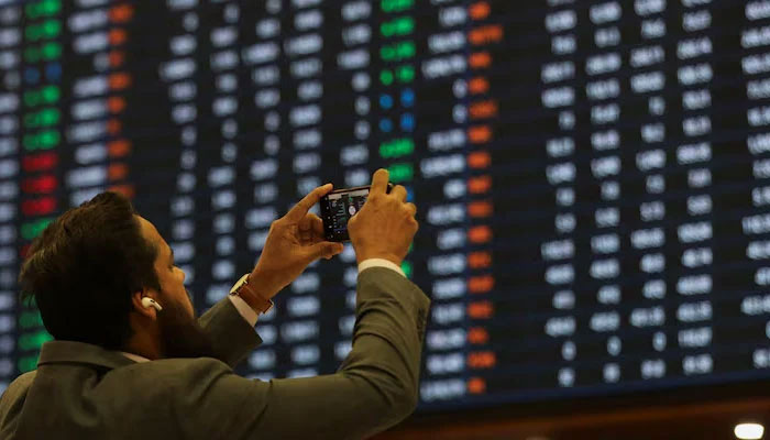 A man uses a mobile phone as he takes a photo of the electronic board displaying share prices during a trading session at the Pakistan Stock Exchange, in Karachi, Pakistan November 28, 2023. — Reuters