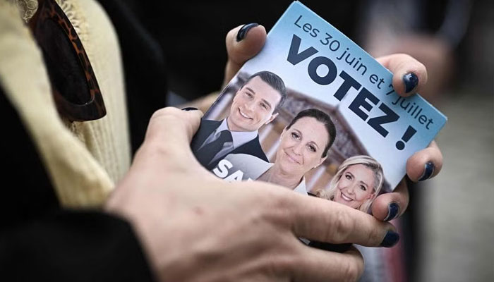A campaigner distributing election leaflets of the French far-right Rassemblement National party at a market in Libourne, southwestern France on July 2, 2024 — AFP