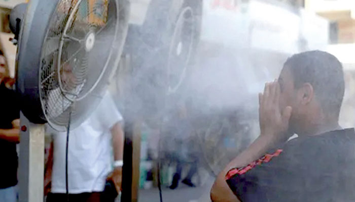 A man cools off as he stands in front of water spray fans placed on the road side as temperatures soar. — AFP/file