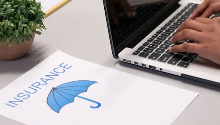 A representational image showing a person using a laptop alongside a paper labelled insurance. — Pexels/File