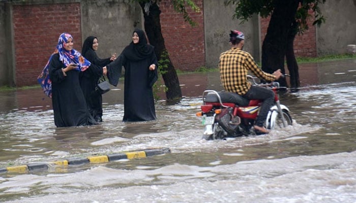 A motorcyclist passes through pedestrians on an inundated road in Lahore on July 21, 2022. — APP