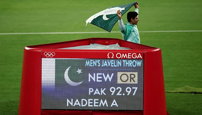 Javelin thrower and Olympic gold medallist Arshad Nadeem holds national flag alongside a screen reflecting the Olympic record set by him.— Reuters/File