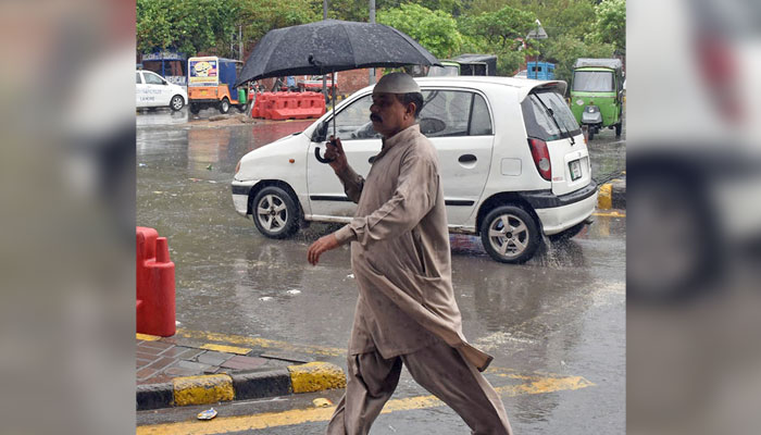 A man holds an umbrella on his way to a road during rain in the morning hours in Lahore on August 20, 2024. — Online