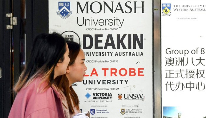 Women walk past signage advertising Australian universities in Melbournes central business district on June 10, 2020. — AFP