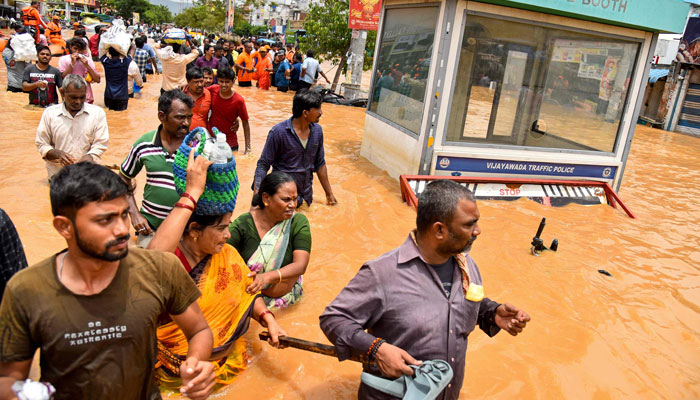 People walk past a police booth as they wade through floodwaters after heavy monsoon rains, along a street in Vijayawada on September 2, 2024. — AFP
