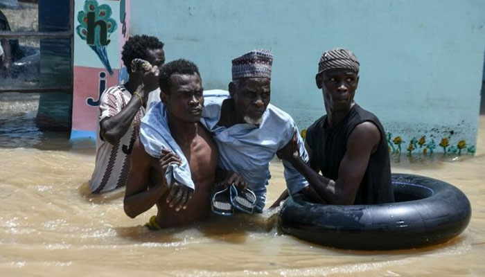 People help an elderly man wade through flood water in Maiduguri on September 12, 2024. — AFP