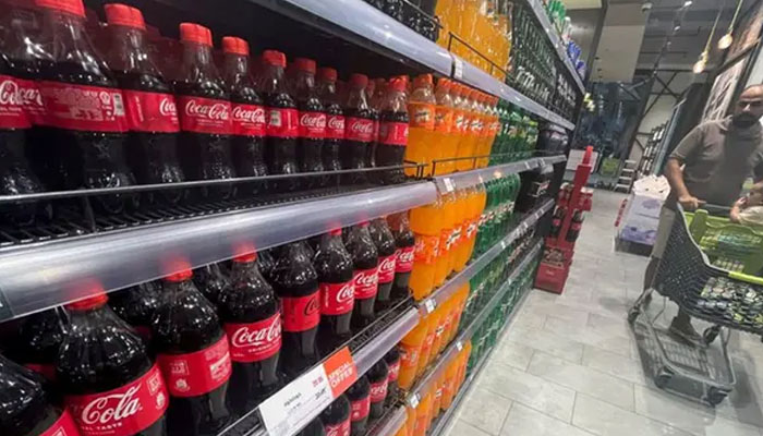 A person walks next to the bottles of Coca-Cola and other products on shelves. — Reuters/File