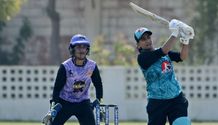 A woman cricketer plays a shot with wicket-keeper in the background.— PCB website/file