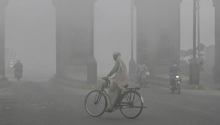 A cyclist rides along a street engulfed in thick smog, in Lahore on November 10, 2024. — AFP