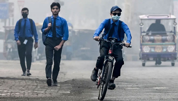 A student wearing a mask rides a bicycle to school along a street engulfed in smog on November 5, 2024. — AFP