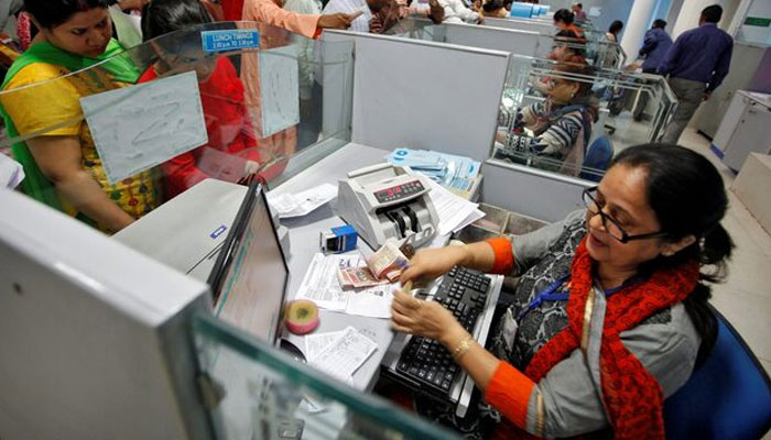 A cashier counts banknotes as customers wait in queues inside a bank. — Reuters/file