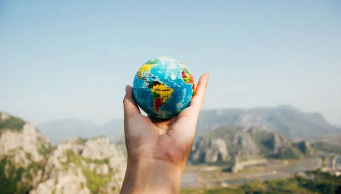 The representational image shows a person holding a world map globe facing a mountain.— Pexels/File
