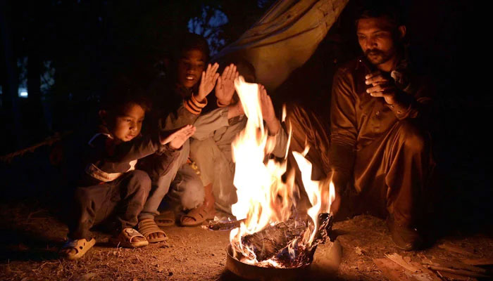 This representational image shows a family sitting around the fire to keep them warm as the temperature falls. — APP/File