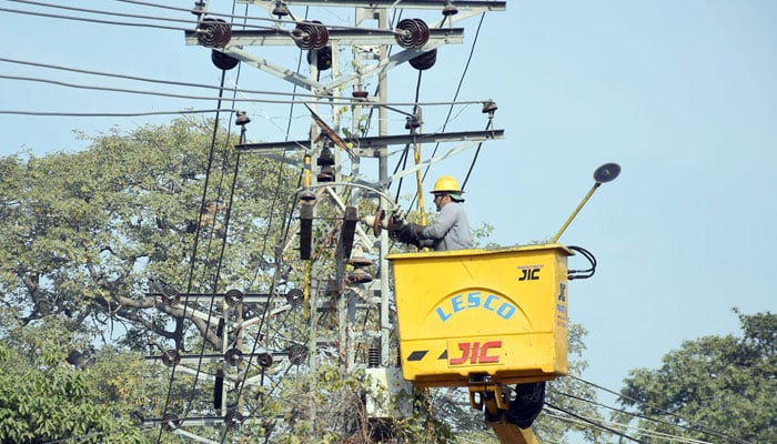 Lesco worker repairs high voltage electric wires on a pole alongside a road, in Lahore on December 9, 2024. — Online