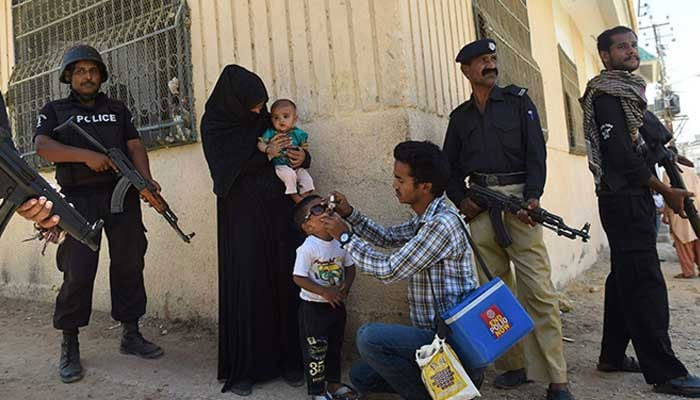 Policemen stand guard as a health worker administers polio drops to a child during a vaccination campaign against the crippling disease. — AFP/File