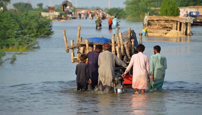 Men walk along a flooded road with their belongings, following rains and floods during the monsoon season in Sohbatpur, August 28, 2022. — Reuters