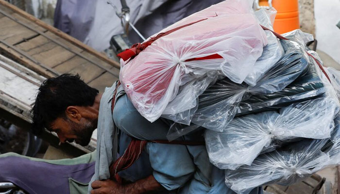 A labourer bends over as he carries packs of textile fabric on his back to deliver to a nearby shop in a market in Karachi on June 24, 2022. — Reuters