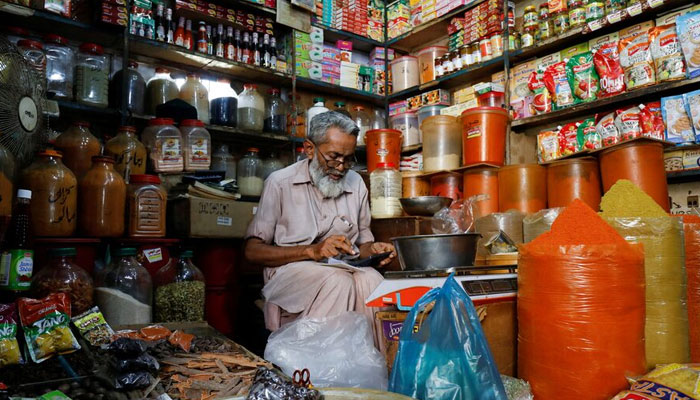 A shopkeeper uses a calculator while selling spices and grocery items along a shop in Karachi on June 11, 2021. — Reuters