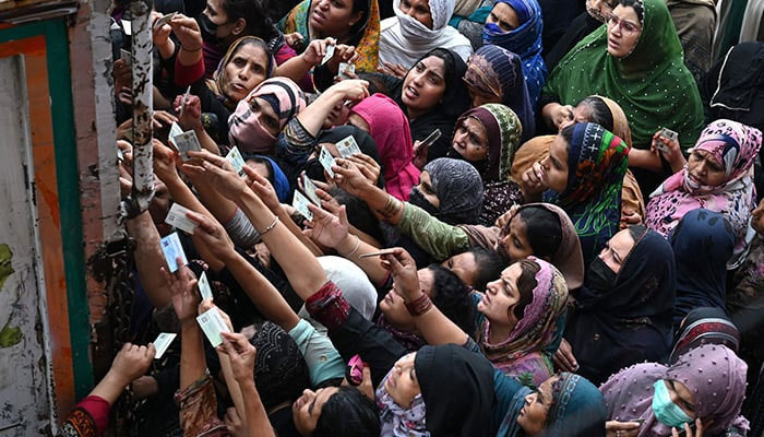 People show their NICs to receive free bags of flour from a delivery truck at a distribution point in Lahore on March 20, 2023. — AFP