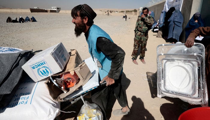 A UNHCR worker pushes a wheelbarrow loaded with aid supplies for a displaced Afghan family outside a distribution center as a Taliban fighter secures the area on the outskirts of Kabul, Afghanistan October 28, 2021. — Reuters