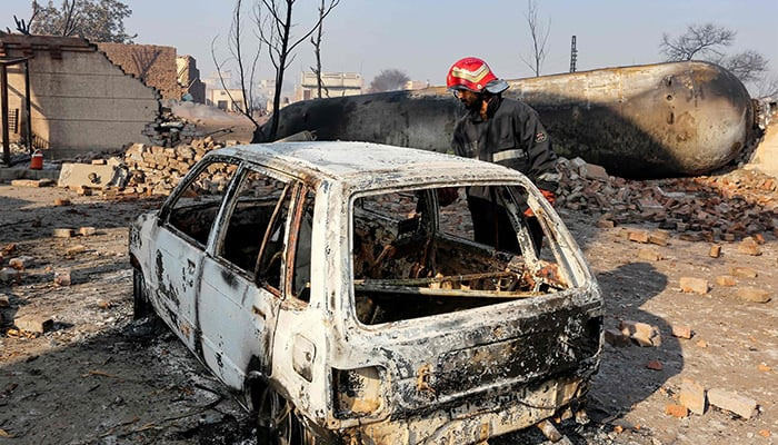 A rescue personnel inspects a charred vehicle, parked near houses destroyed after an LPG tanker truck exploded near an industrial area in Multan on January 27, 2025. — AFP