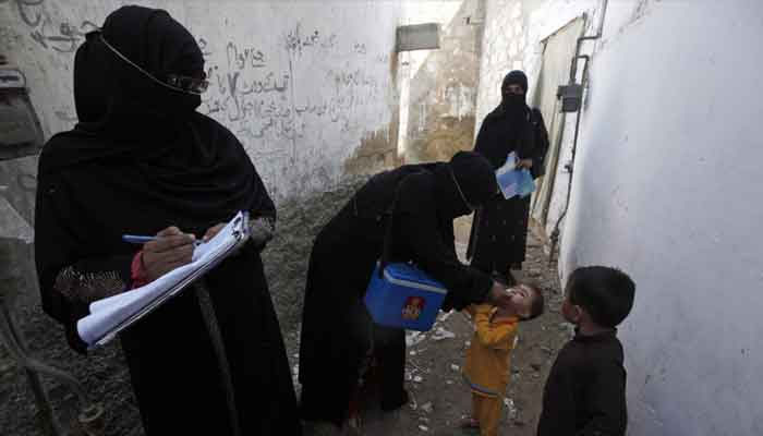 A polio vaccinator (centre) administers polio vaccine drops to a boy while a colleague takes notes nearby, along a street in a Karachi slum. — Reuters/File