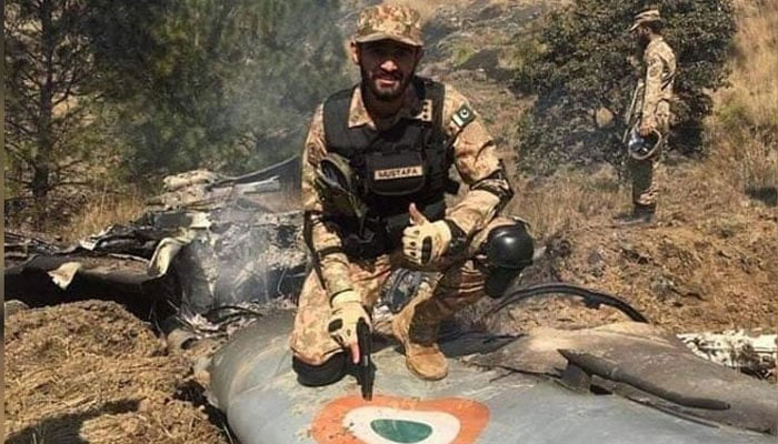 A Pakistan Army soldier poses for a photo while sitting on the debris of an Indian fighter jet shot down by PAF on February 27, 2019. — Radio Pakistan