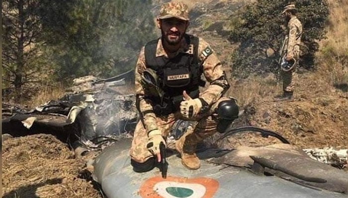 A Pakistan Army soldier poses for a photo while sitting on the debris of an Indian fighter jet shot down by PAF on February 27, 2019. — Radio Pakistan