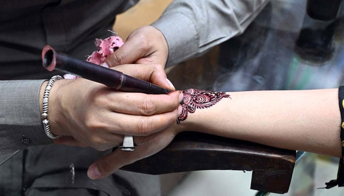 Artisan applies henna to girls hands as they prepare for Eid ul Fitr celebrations on March 30, 2025. — APP