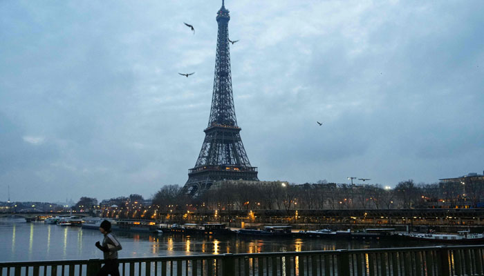 A resident runs on the snow-covered bridge of Grenelle in Paris, with the Eiffel Tower seen in the background, on January 18, 2024. — AFP