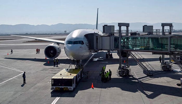 Ground staff stand next to the Pakistan International Airline (PIA) aircraft ahead of its takeoff on January 10, 2025. — AFP