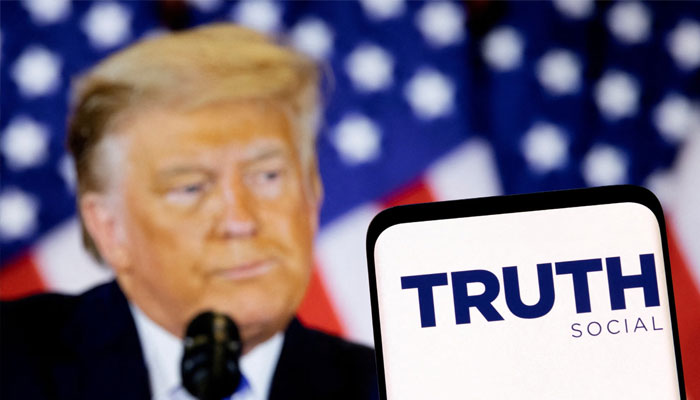 The Truth social network logo is seen on a smartphone in front of a display of US President Donald Trump in this picture illustration taken February 21, 2022. — Reuters
