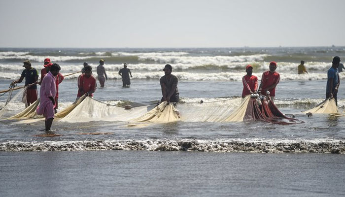 This representational image of fishermen pull a fishing net ashore at the Clifton beach in Karachi. — AFP/File