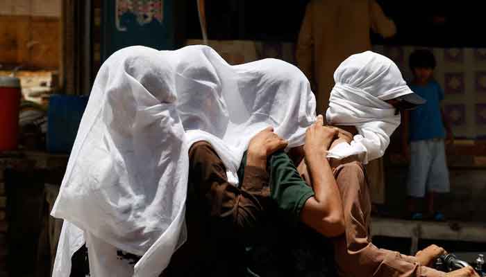 Men ride on a motorbike as they cover their heads with a wet cloth to cool off and to avoid sunlight, during a hot summer day, as the heatwave continues in Jacobabad, May 26. — Reuters/File